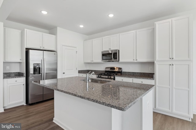 kitchen featuring dark wood-style flooring, dark stone counters, white cabinets, a sink, and appliances with stainless steel finishes