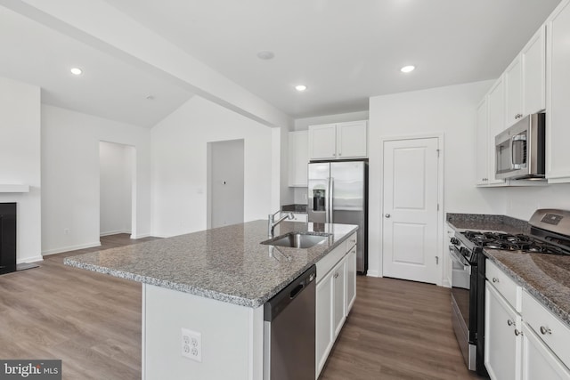 kitchen with a sink, dark stone counters, stainless steel appliances, white cabinetry, and an island with sink