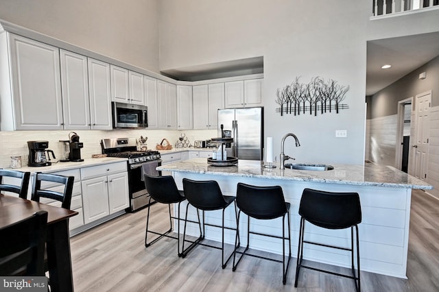 kitchen featuring a breakfast bar area, light wood-type flooring, a sink, a high ceiling, and stainless steel appliances