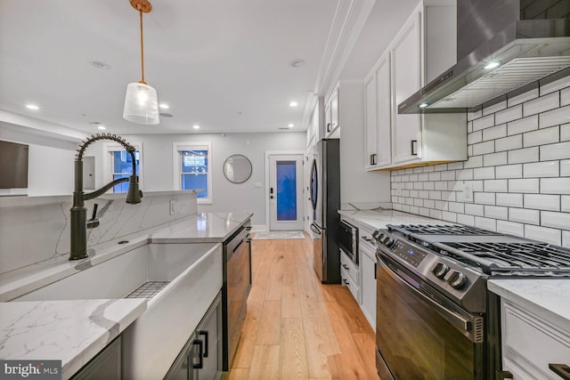 1317 Randolph St NW Unit 1, Washington, DC 20011 - kitchen with wall chimney range hood, decorative light fixtures, appliances with stainless steel finishes, light wood-style floors, and white cabinetry
