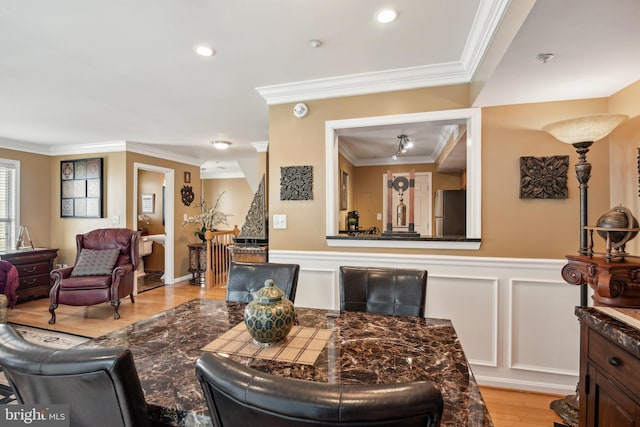 living room with a decorative wall, ornamental molding, a wainscoted wall, and light wood-style floors