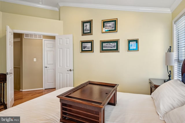 bedroom featuring baseboards, ornamental molding, wood finished floors, and visible vents