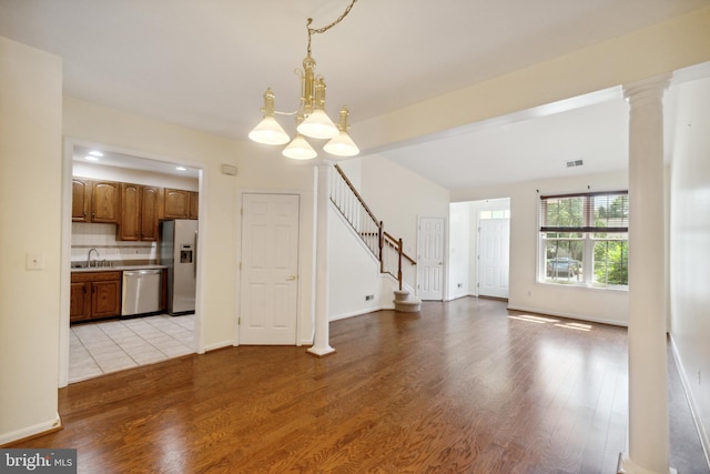unfurnished living room with stairs, a chandelier, a sink, and light wood-style floors