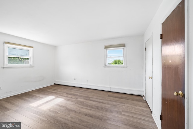 unfurnished bedroom featuring baseboards, a baseboard heating unit, multiple windows, and wood finished floors