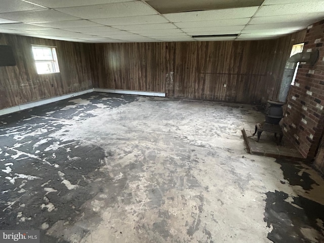 below grade area featuring a wood stove, a drop ceiling, and wooden walls