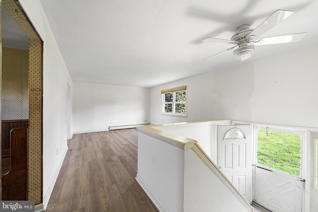 hallway with wood finished floors, baseboards, a baseboard heating unit, and an upstairs landing