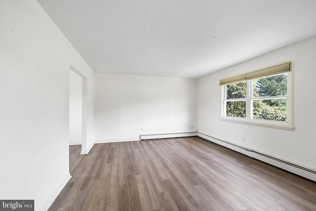 empty room featuring baseboards, a baseboard heating unit, and wood finished floors