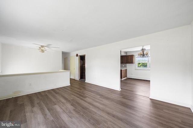 unfurnished living room featuring baseboards, ceiling fan with notable chandelier, and dark wood-type flooring