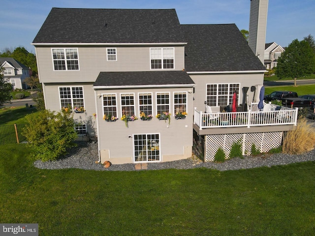 back of property with a yard, a wooden deck, roof with shingles, and a chimney