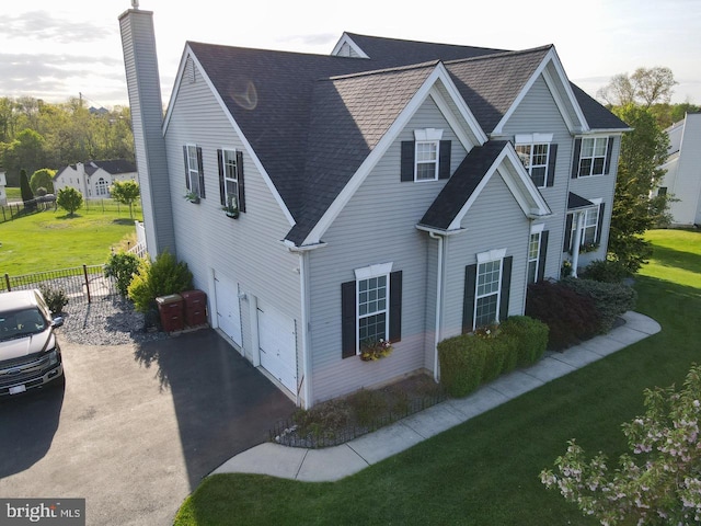 view of property exterior featuring fence, aphalt driveway, a garage, a chimney, and a yard