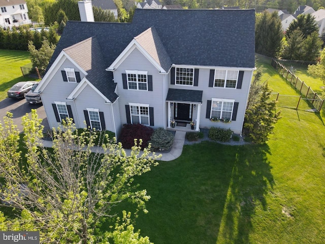 view of front of house with a front yard, fence, a chimney, and roof with shingles