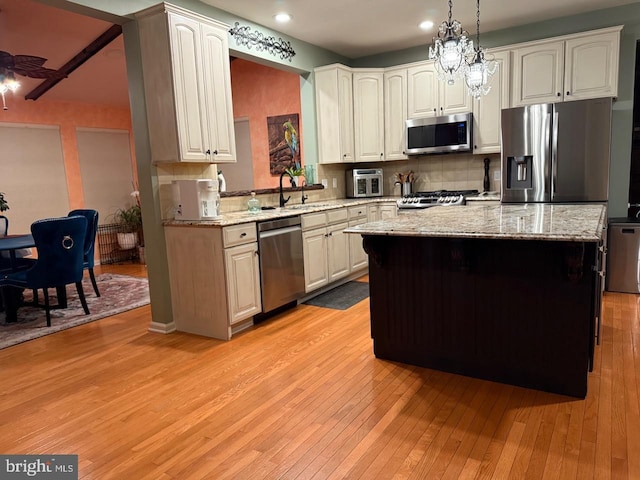 kitchen featuring backsplash, appliances with stainless steel finishes, a center island, a sink, and light wood-style floors