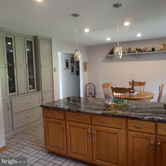 kitchen featuring brown cabinetry, brick patterned floor, dark stone countertops, and decorative light fixtures