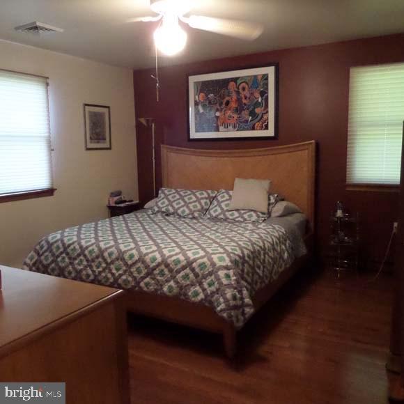 bedroom with ceiling fan, visible vents, and wood finished floors