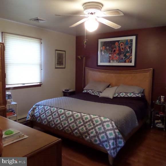 bedroom with ceiling fan, visible vents, and wood finished floors