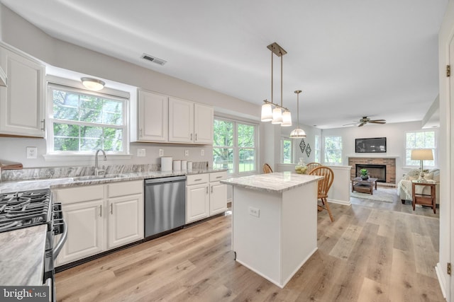 kitchen featuring appliances with stainless steel finishes, a sink, a fireplace with raised hearth, white cabinets, and plenty of natural light