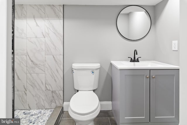 full bathroom with vanity, baseboards, a tile shower, and toilet