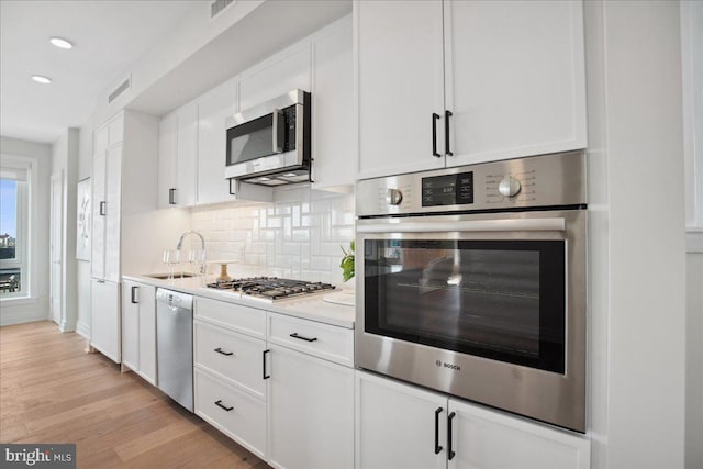 923 V St NW Unit 601, Washington, DC 20001 - kitchen featuring stainless steel appliances, white cabinets, tasteful backsplash, light countertops, and light wood-style floors