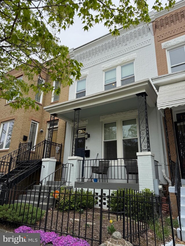 townhome / multi-family property with a porch, brick siding, and a fenced front yard