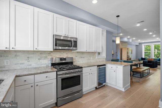 kitchen featuring stainless steel appliances, wine cooler, open floor plan, a peninsula, and white cabinetry