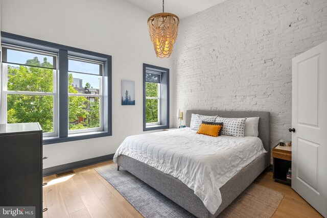 bedroom with a chandelier, a towering ceiling, wood finished floors, and brick wall