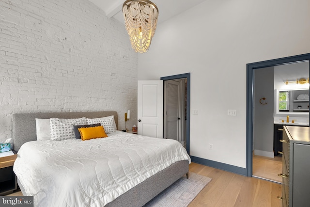 bedroom featuring a towering ceiling, light wood finished floors, a chandelier, baseboards, and beam ceiling