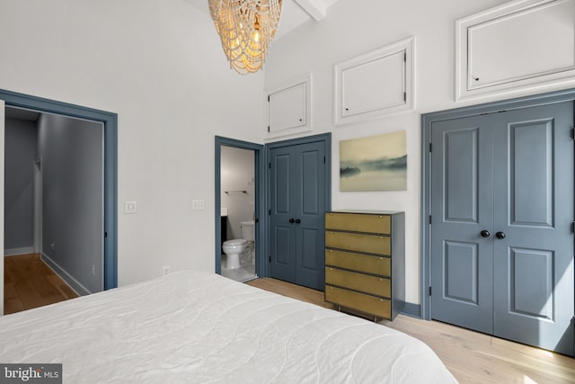 bedroom featuring a chandelier, wood finished floors, a high ceiling, ensuite bath, and baseboards