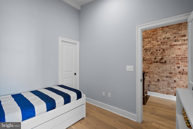 bedroom with wood finished floors, baseboards, and brick wall