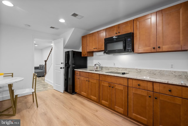 kitchen with black appliances, light wood-style flooring, a sink, brown cabinets, and recessed lighting