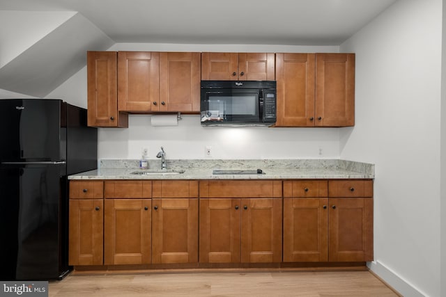 kitchen with black appliances, a sink, light wood-type flooring, light stone counters, and brown cabinetry