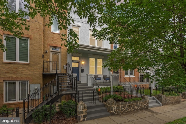 multi unit property with stairs, brick siding, a porch, and a fenced front yard