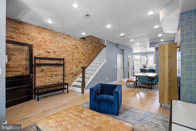 sitting room with stairs, light wood-style flooring, recessed lighting, baseboards, and brick wall