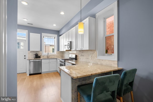 kitchen featuring stainless steel appliances, tasteful backsplash, white cabinets, light stone countertops, and a peninsula
