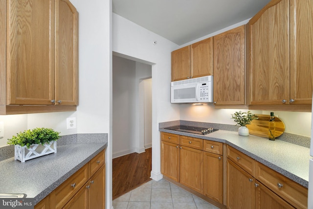 6704 Holly Farm Ln Unit 203, New Baltimore, VA 20187 - kitchen with white microwave, black electric stovetop, light tile patterned floors, baseboards, and brown cabinets