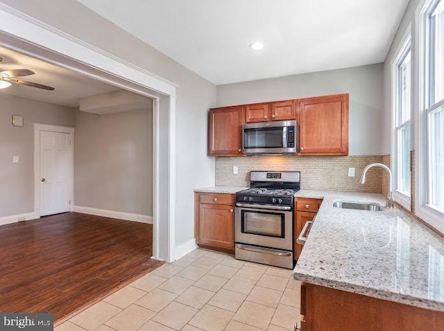 65 N Monastery Ave, Baltimore, MD 21229 - kitchen with brown cabinetry, backsplash, a sink, light stone counters, and stainless steel appliances