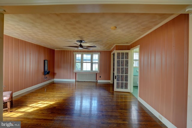 spare room with radiator heating unit, ornamental molding, wood finished floors, baseboards, and wood walls