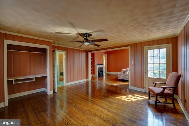 living area with ornamental molding, wood finished floors, baseboards, ceiling fan, and wood walls