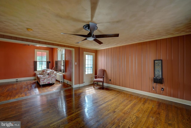 living area featuring a ceiling fan, radiator, baseboards, wood finished floors, and ornamental molding