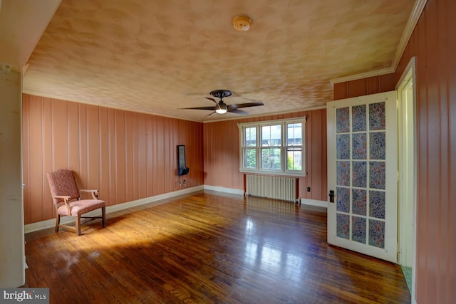unfurnished room with radiator, ceiling fan, wood finished floors, baseboards, and crown molding