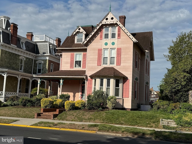 victorian-style house featuring a front lawn, a shingled roof, and a chimney
