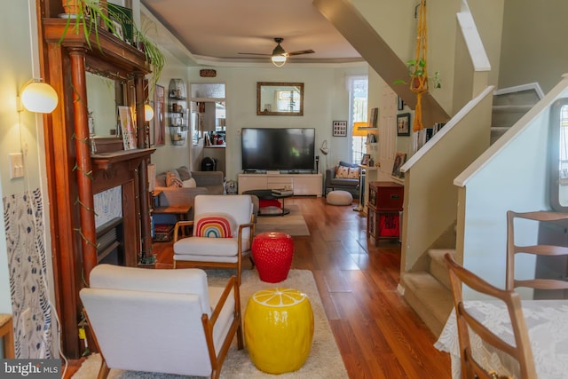 living room featuring a ceiling fan, stairs, a glass covered fireplace, and wood finished floors