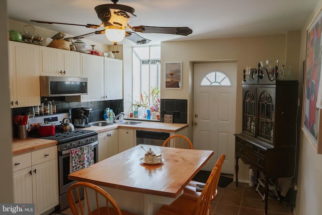 kitchen featuring a ceiling fan, wood counters, dark tile patterned flooring, appliances with stainless steel finishes, and tasteful backsplash