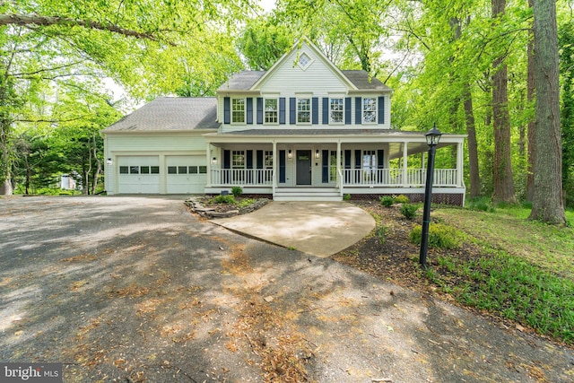 colonial home with an attached garage, a shingled roof, covered porch, and driveway