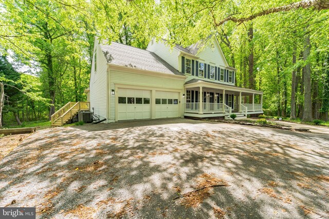 colonial-style house with a shingled roof, an attached garage, central AC, aphalt driveway, and a porch