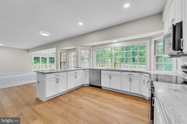 kitchen with white cabinetry, light stone counters, a sink, light wood finished floors, and stainless steel appliances