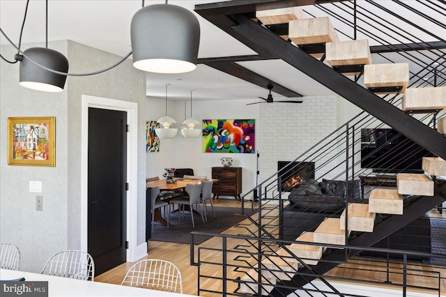 living room with a ceiling fan, a brick fireplace, wood finished floors, a textured wall, and stairs