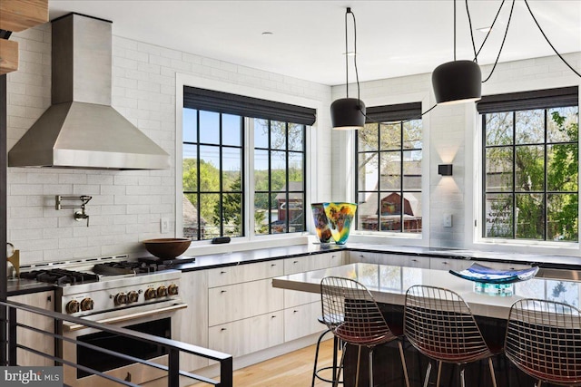 kitchen with wall chimney range hood, tasteful backsplash, plenty of natural light, and high end stainless steel range oven