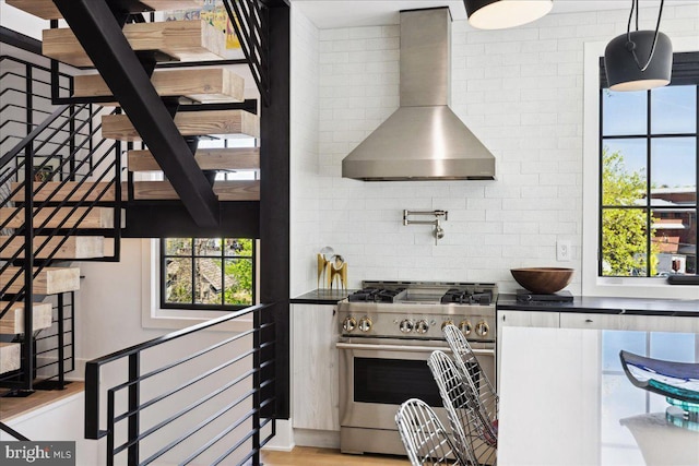 kitchen with high end range, backsplash, dark countertops, and wall chimney range hood