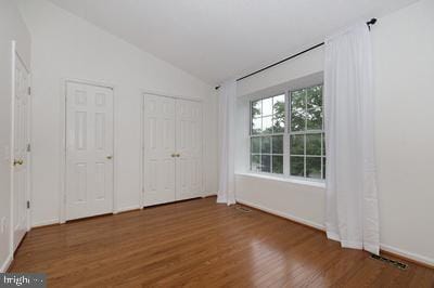 unfurnished bedroom featuring lofted ceiling, baseboards, multiple closets, and wood finished floors