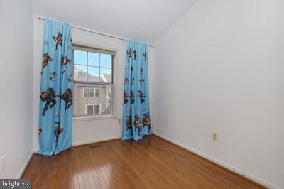 unfurnished room featuring vaulted ceiling, wood finished floors, and baseboards